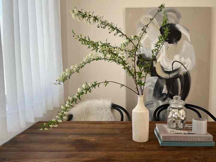 ベージュの壁の寝室、ヴィンテージの木目調テーブルに花瓶とモダンアートが配置された雰囲気のあるインテリア