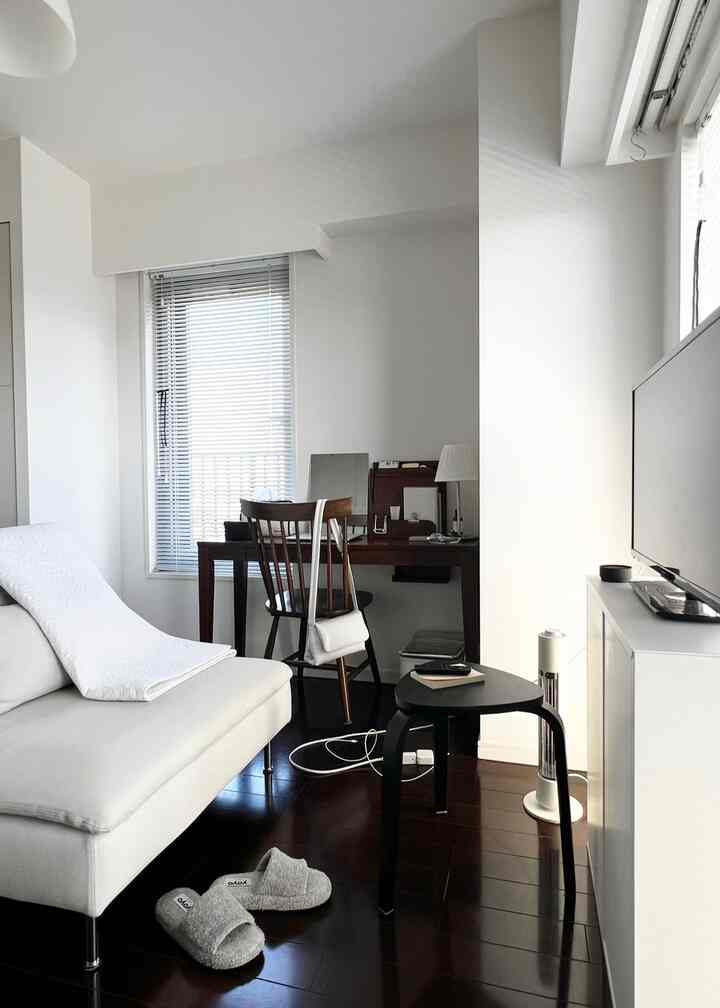 明るいホワイトトーンのコンパクトなリビング、ソファと木製デスク、ブラインドが配置されたモダンなインテリア