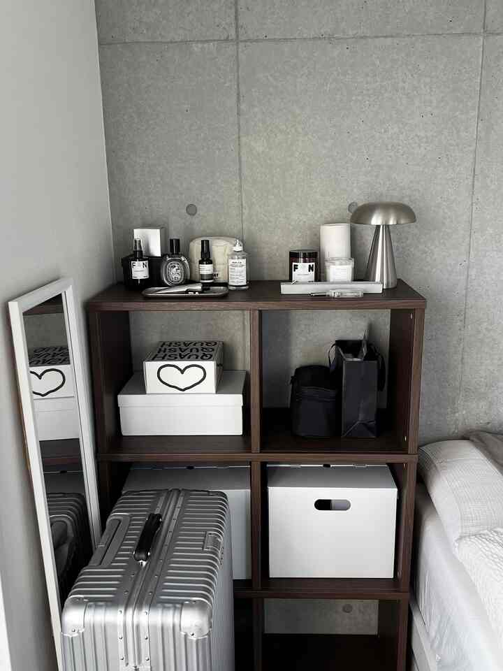 ナチュラルカラーとシルバーのトーンが調和した寝室の一角、木製キャビネット、シルバーのスーツケースとテーブルランプが置かれたモダンで整ったインテリア
