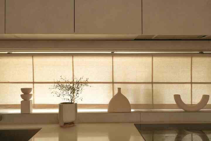 ベージュのトーンのキッチン空間で、ストーンテクスチャーのカウンターとベージュカーテン、陶器のオブジェが調和したモダンな雰囲気のインテリア