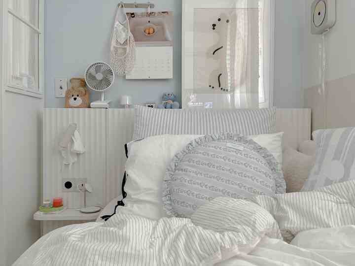 白とグレーのトーンの寝室、ストライプの寝具と額縁が配置されたシンプルで落ち着いたインテリア