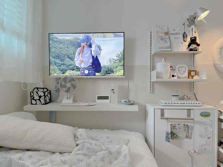 白を基調とした寝室、ベッドとデスク、壁掛けテレビが配置された印象的でミニマルな空間