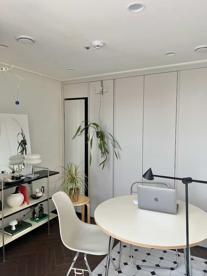 白と木目調のウォークインクローゼット兼ホームオフィス、ラウンドテーブルと植物が配置された清潔感のある作業空間