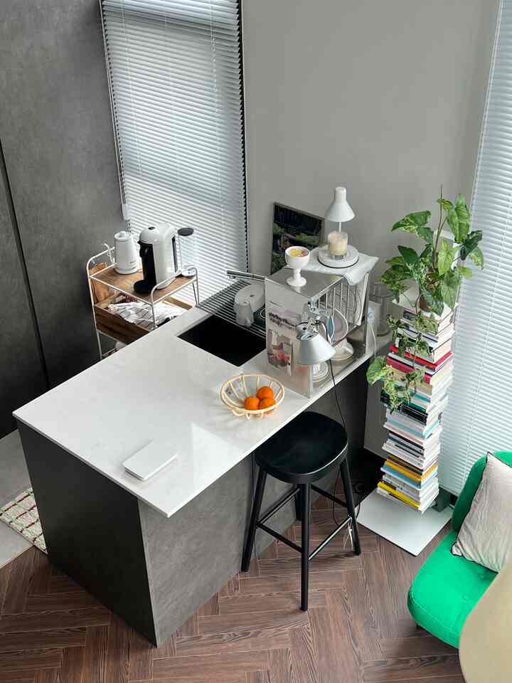 グレーの壁とホワイトのキッチンアイランドが配置されたナチュラルなトーンのキッチン、バースツールと本棚がある雰囲気のあるインテリア