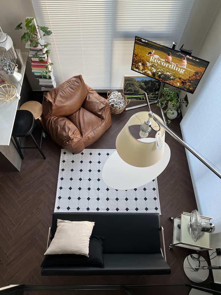 ナチュラルカラーの居心地の良いリビング、ブラウンのビーズクッションチェアと黒いソファ、白いブラインドが配置されたモダンなインテリア