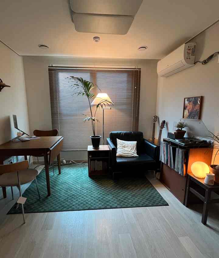 温かみのある木目調とグリーンが調和する小さなホームオフィス、木製家具とヴィンテージラグ、照明が配された落ち着いたインテリア