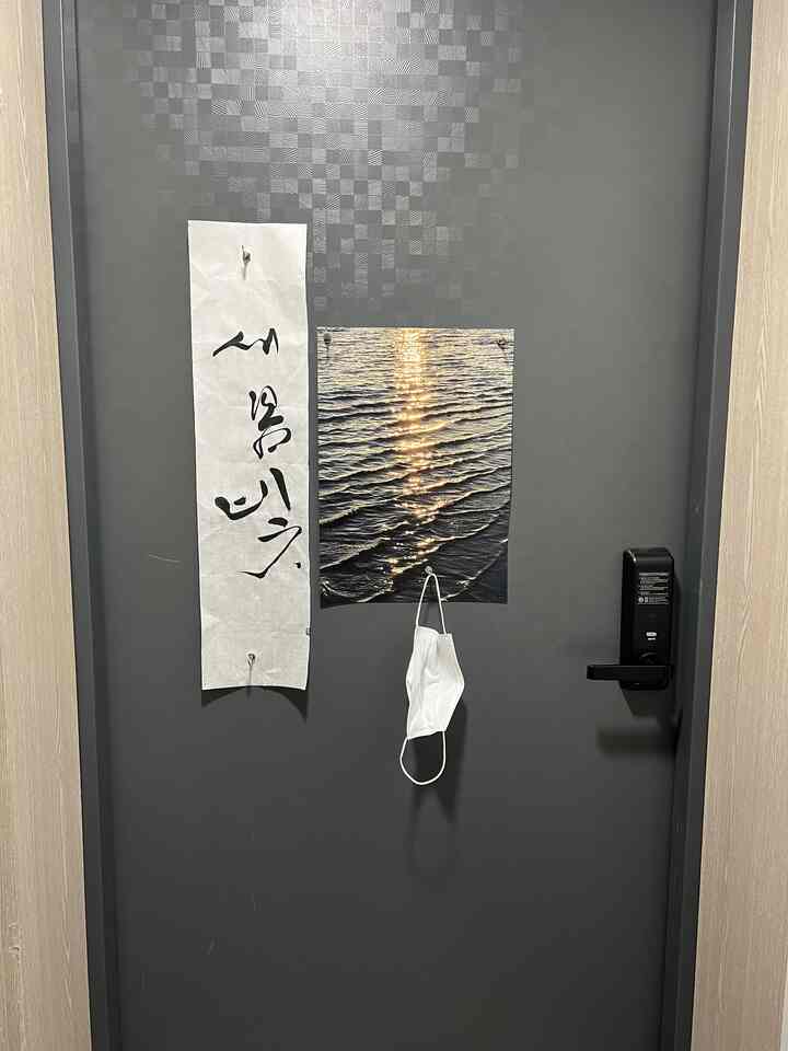 黒を基調とした玄関のドアに、春の書道作品と海のポスターが飾られたシンプルな空間