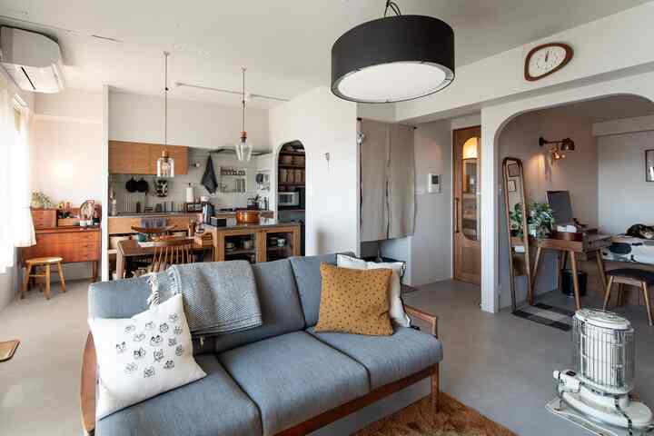 白とグレーのトーンのリビングルーム、モダンでナチュラルなスタイルで3人掛けソファとキッチン、ダイニングテーブルが配置された印象的な空間