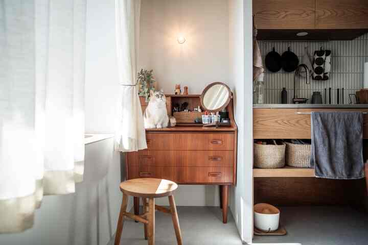 ナチュラルカラーと木目調が調和するキッチン隣のメイクスペースで、ヴィンテージのドレッサーと猫がいる雰囲気のある空間