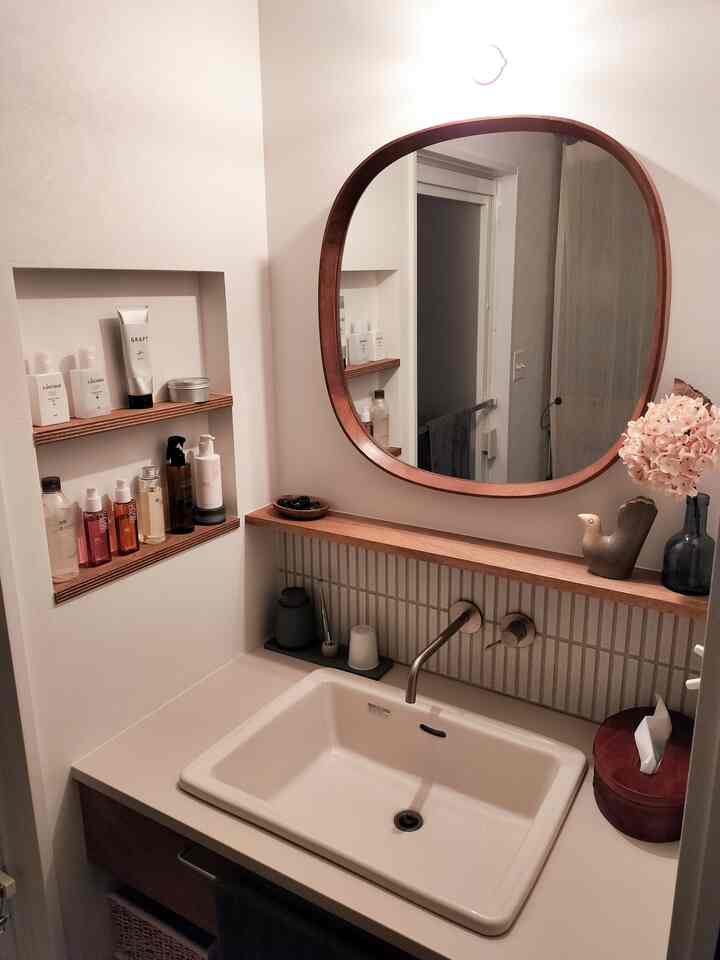 白い壁と茶色の木製家具が調和した洗面台と鏡、収納棚が配置された清潔感のある浴室空間