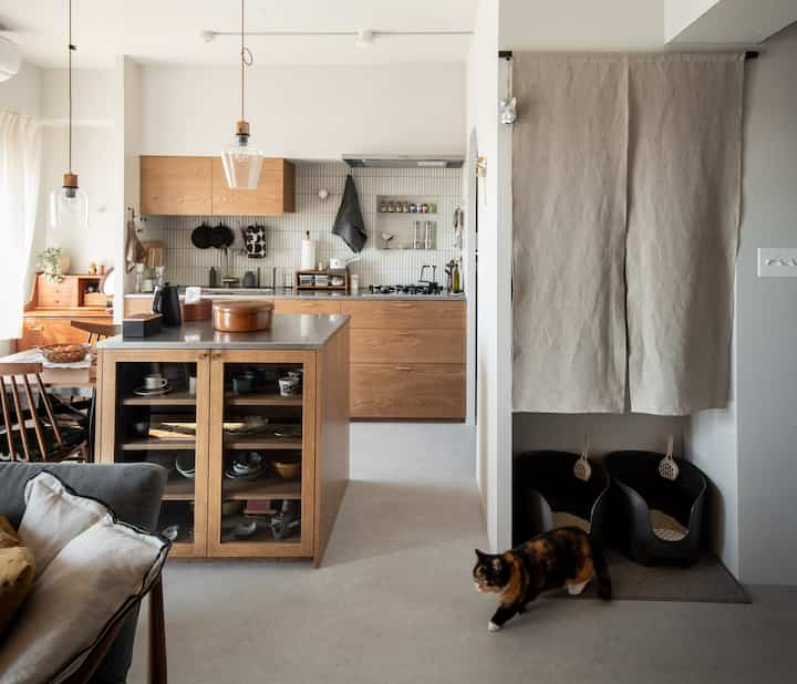 木目調と白色が調和したキッチンとリビングの空間、窓際に配置された猫のトイレがある雰囲気の良いインテリア