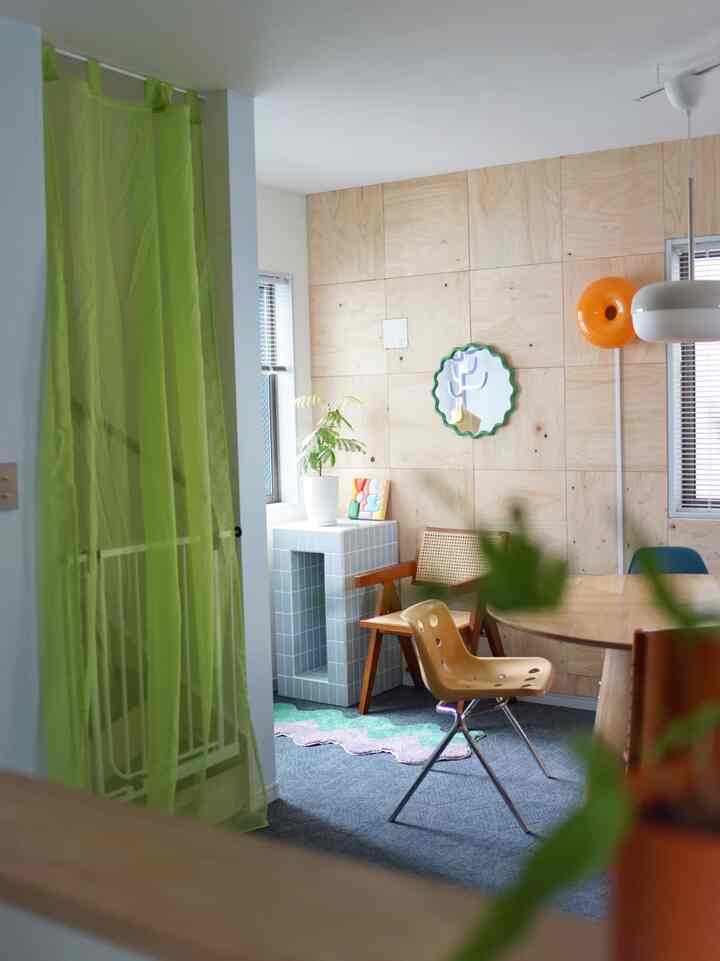 ナチュラルな木目パネルと丸いダイニングテーブル、明るいグリーンのカーテンがあるダイニングルーム