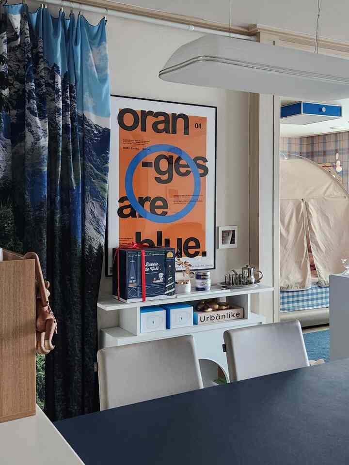 ナチュラルカラーとブルーの色調のダイニングルーム、山のプリントカーテンと白い棚、ベージュのダイニングチェアが配置された雰囲気のある空間