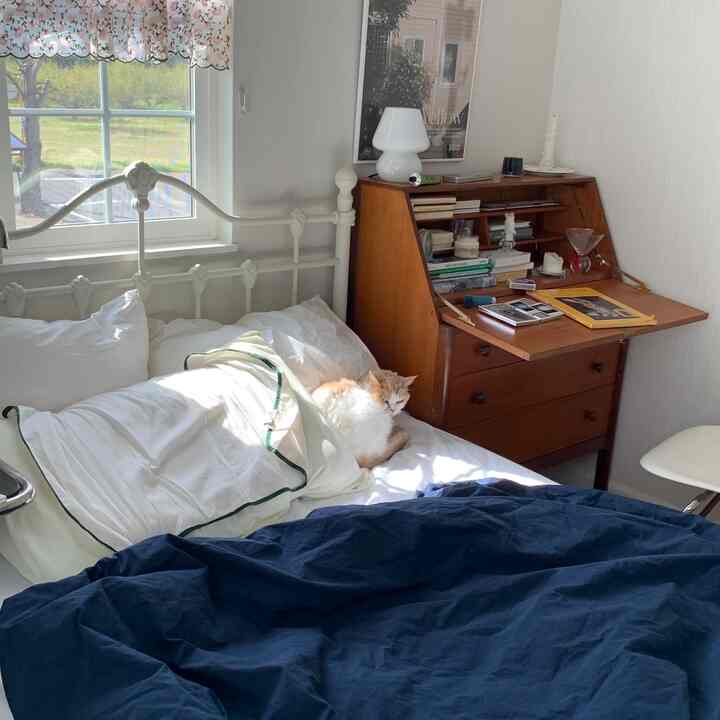 白とネイビーの色調の寝室、窓際のベッドと木製デスクが配置された雰囲気のある空間