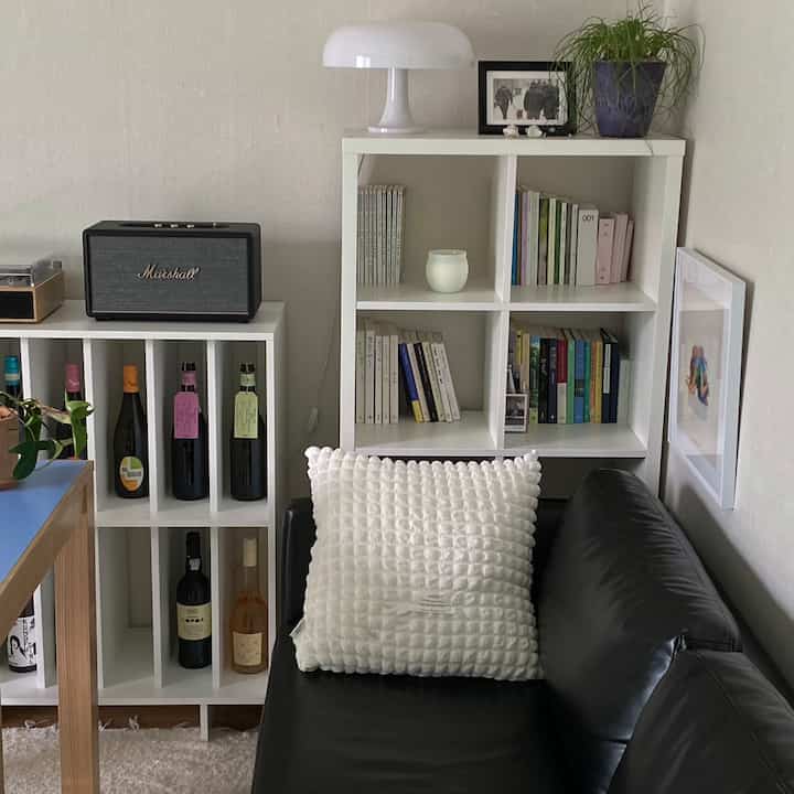 白と黒のトーンのミニマルなリビング、黒いレザーソファと白い本棚、ワインラックが配置された雰囲気のあるインテリア