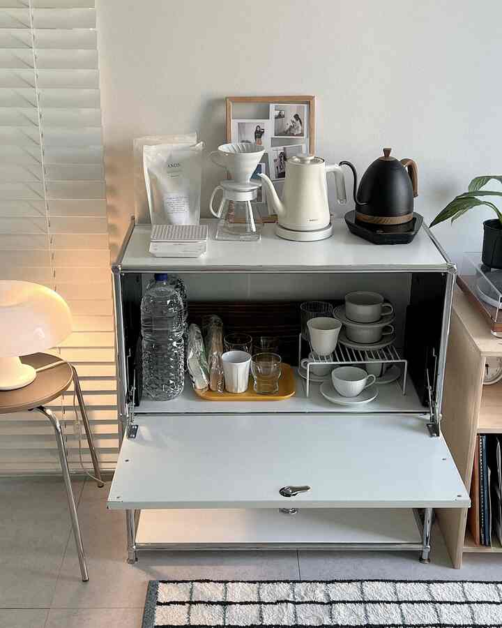 白と黒のシンプルモダンなホームカフェ空間、電気ドリップケトルとドリップコーヒーセットが美しく並べられた収納キャビネットが配置された印象的なインテリア