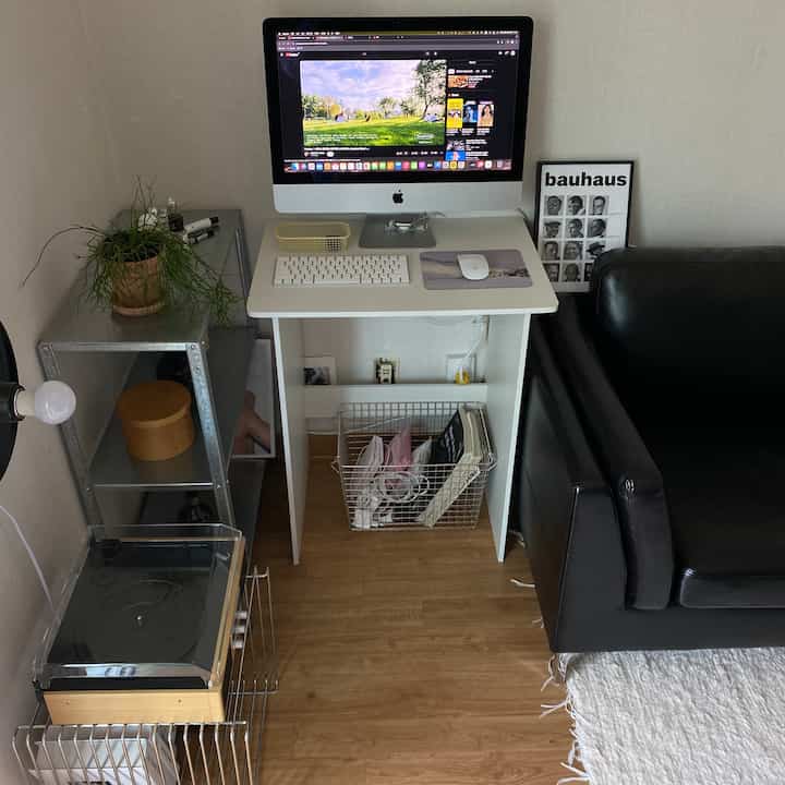 ナチュラルな木目調の床とブラックレザーソファがあるコンパクトなリビングのホームオフィス