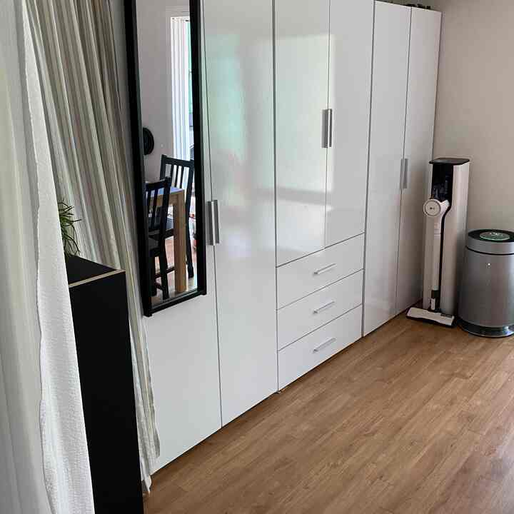 ホワイトトーンの寝室、ブラックフレームの全身鏡が配置され、木目調の床とすっきりした収納家具がある雰囲気のあるインテリア