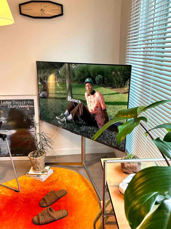 オレンジのラグとシルバー脚のテレビ台があるモダンなリビング、自然光とブラインドが調和した空間