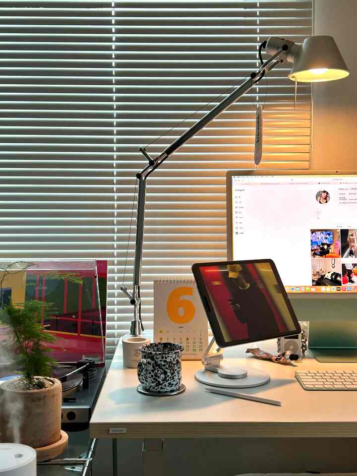 ホワイトトーンのホームオフィス空間、デスク上にアイパッド、モニター、スタンドランプが配置された清潔感のある作業スペース