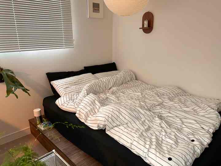 ナチュラルな色調の狭い寝室、低い木製のベッドフレームとストライプの寝具が配置された落ち着いた空間