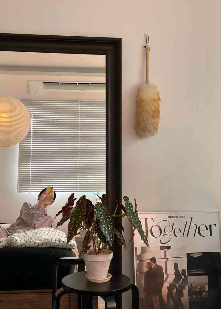 ベージュの壁と黒いフレームの全身鏡がある寝室、植物が置かれた小さな黒いテーブルと温かみのある自然な雰囲気のインテリア