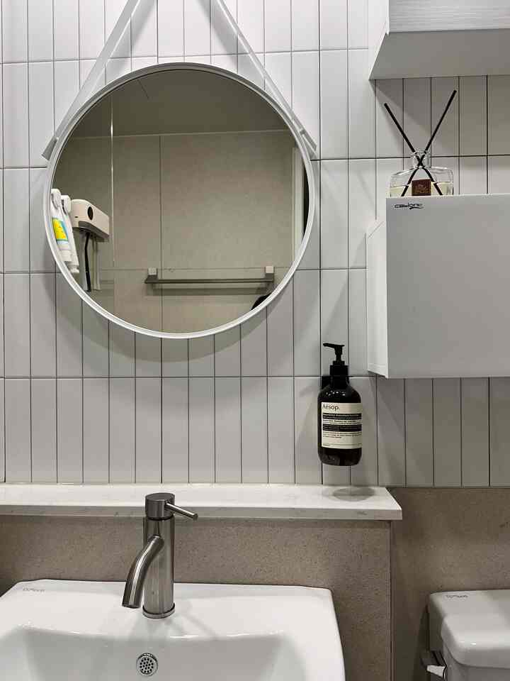 白いタイル壁と丸い鏡、ミニマルな洗面台が配置された清潔感のあるバスルーム