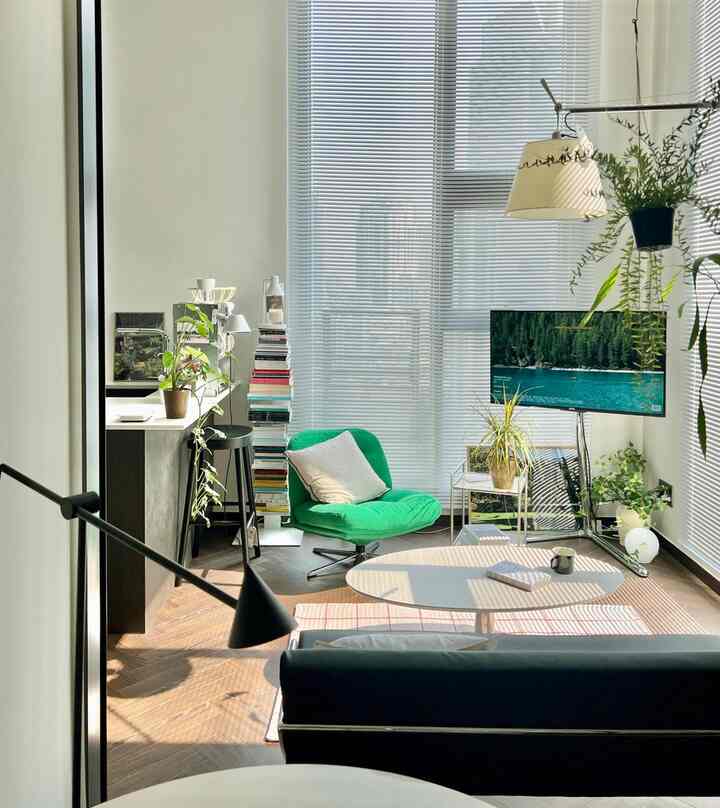 白い壁とナチュラルな木製フロアのリビング、緑のアームチェアと多くの植物が配置されたモダンで自然なインテリア