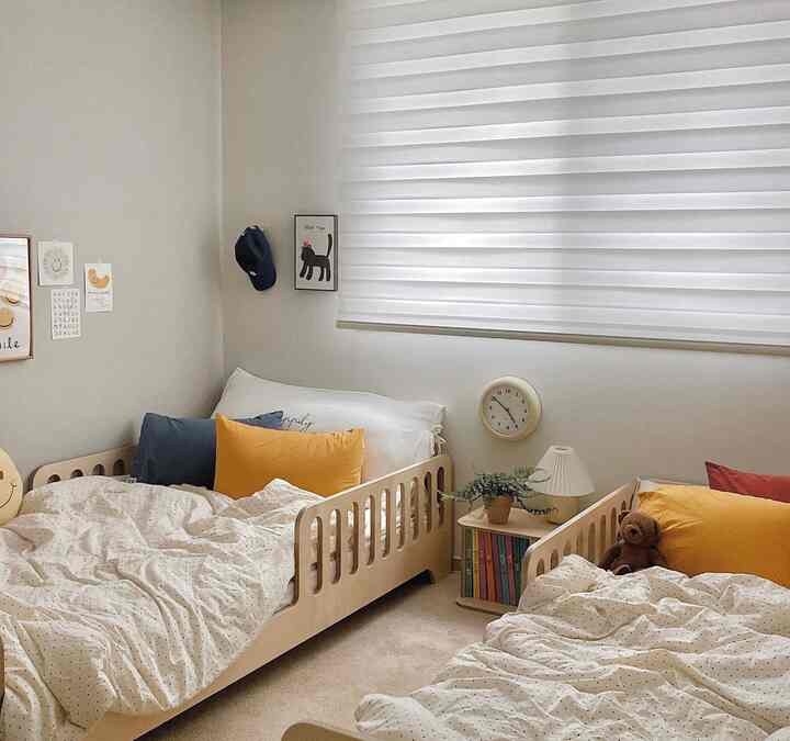 ベージュと白を基調とした子供部屋、2つの子供用ベッドと壁時計、本棚が配置された雰囲気のあるインテリア