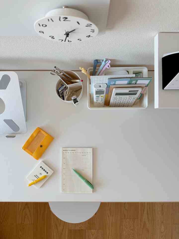 白色のトーンと木目調の床が調和したコンパクトなホームオフィス、整頓されたデスクと文具が配置された実用的な作業空間