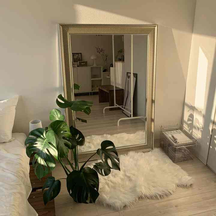 暖かいナチュラルな色調の寝室、中央右に大きなイケアの鏡と緑の植物が調和した印象的な空間