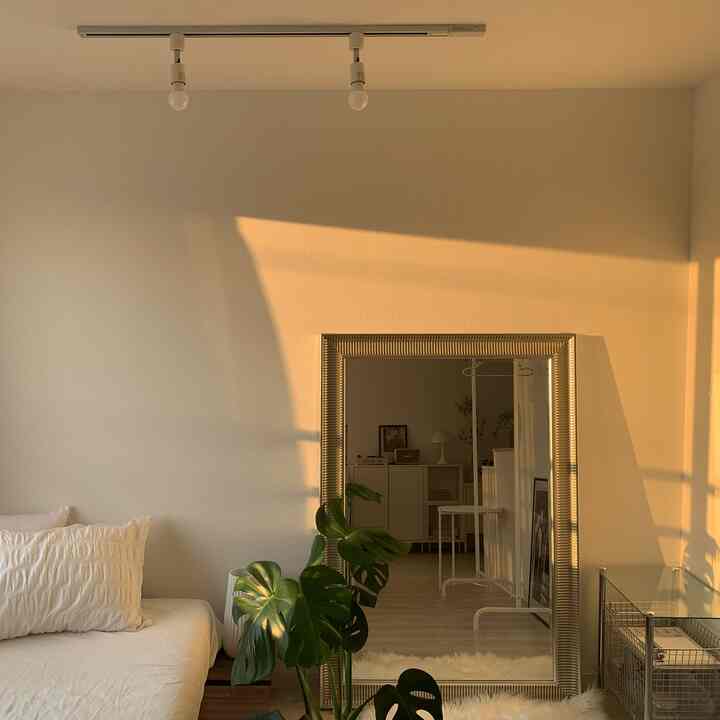 暖かなオレンジ色の自然光が差し込む寝室、シルバーの鏡とベッドフレーム、グリーンの植物が配置された雰囲気のあるインテリア