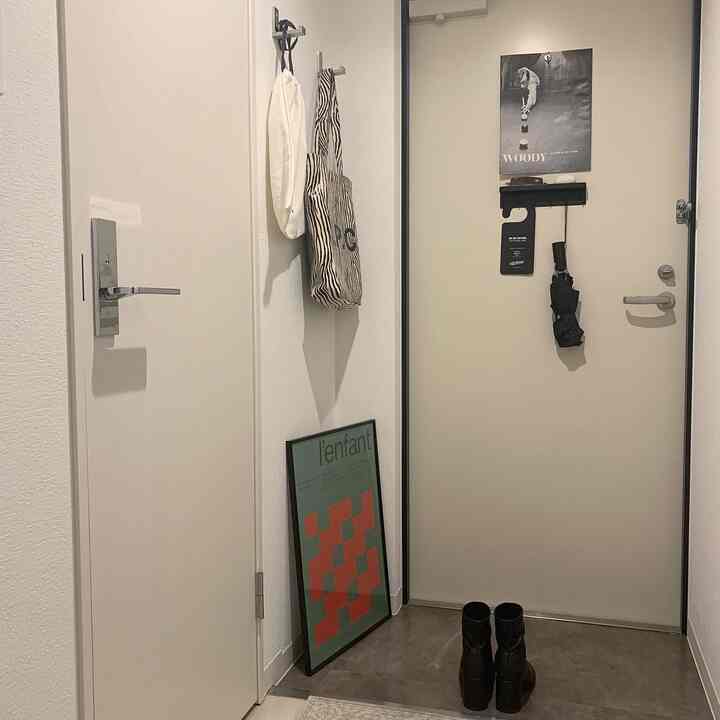 白とベージュの狭い玄関、壁にポスターとマグネットキーフックが配置された清潔感のあるミニマルなインテリア