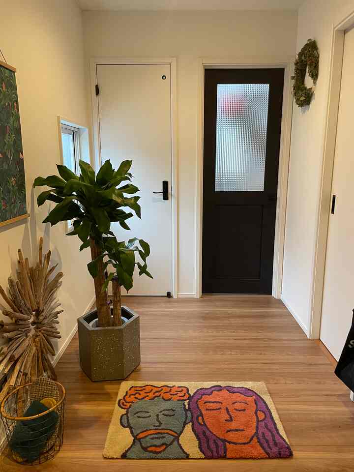 白壁とナチュラルな木目調の床が広がる玄関、アートポスターと大きな観葉植物が配置された温かみのある空間