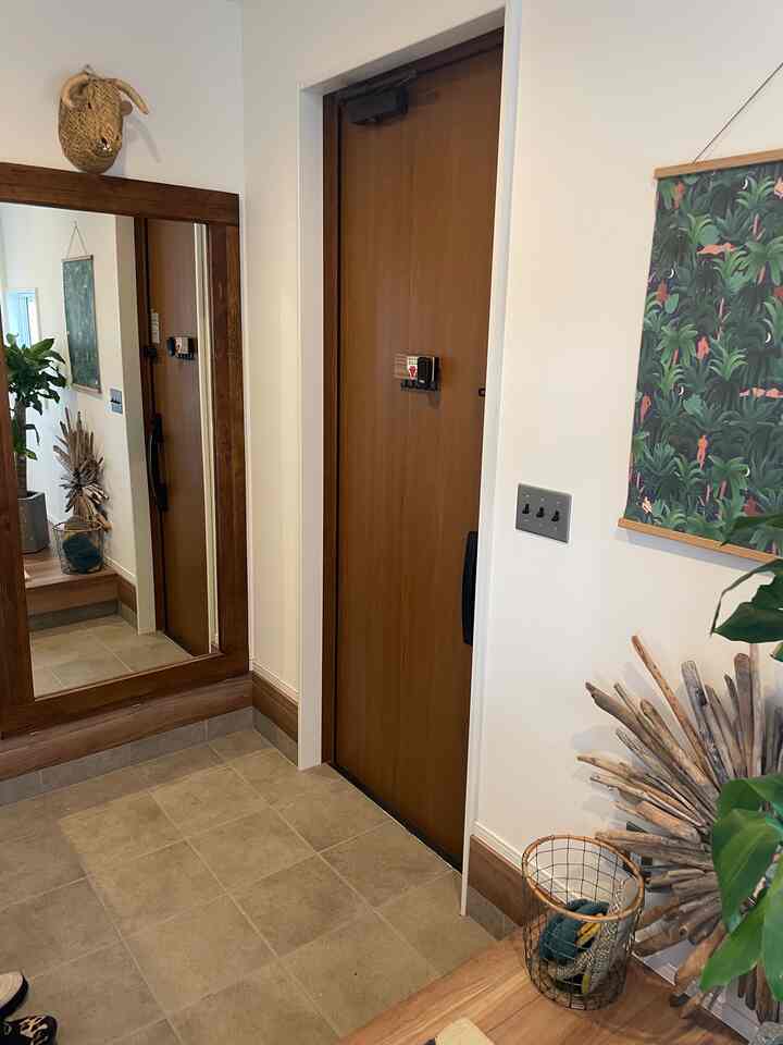 ナチュラルな木目調の壁と大きな鏡、ポスターが配置された清潔感のある玄関スペース