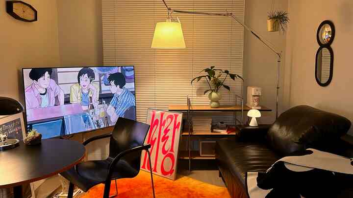 モダンなブラック家具とオレンジのラグが印象的なリビング、ブラインドと多様な照明が居心地の良い雰囲気を演出