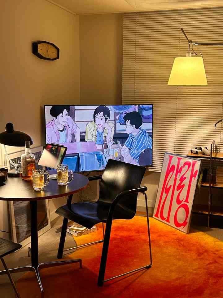 温かみのあるオレンジのラグと黒い家具が調和するリビング、ホームバー風のテーブルとテレビが配置された雰囲気ある空間