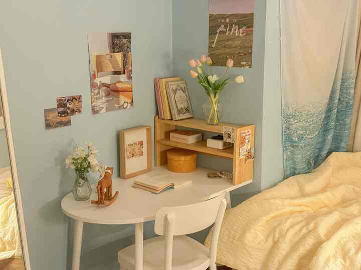 白と青のトーンの寝室の一角、デスクと木製の棚、黄色の寝具が温かみのある雰囲気を作る空間