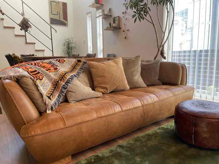 暖かいブラウン調のリビング、レザーソファとヴィンテージ風のオットマンが配置された自然な雰囲気のインテリア