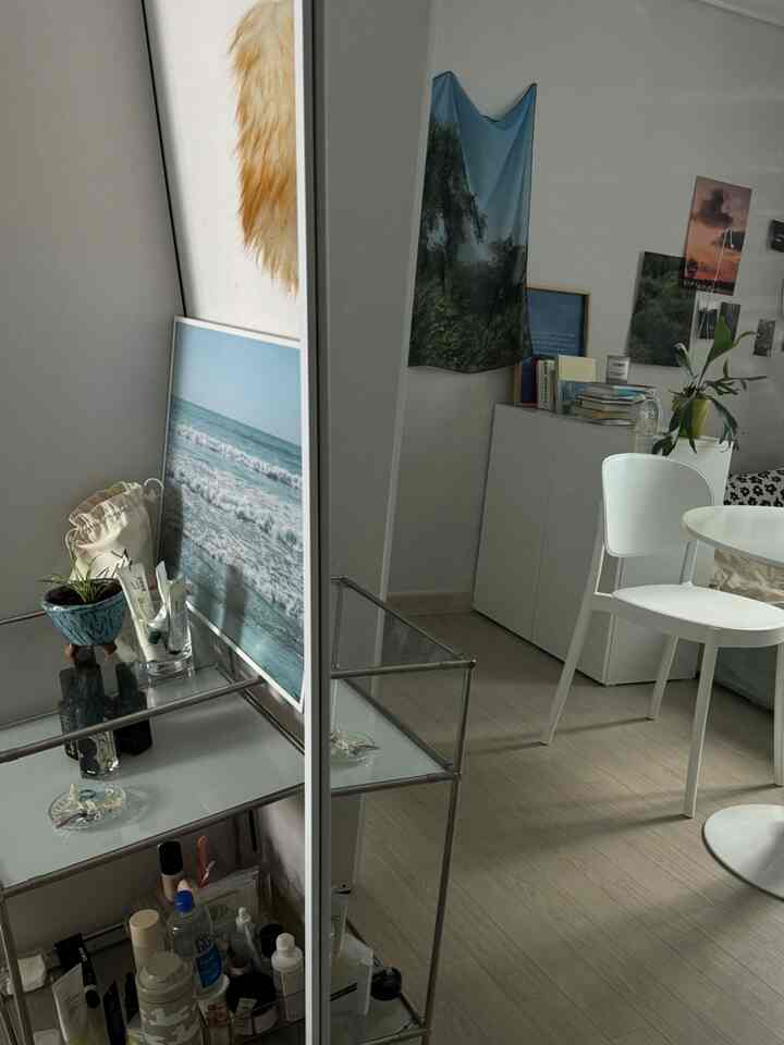 白とナチュラルカラーの狭い部屋、全身鏡とガラス棚、丸いダイニングテーブルと椅子が配置された印象的な空間