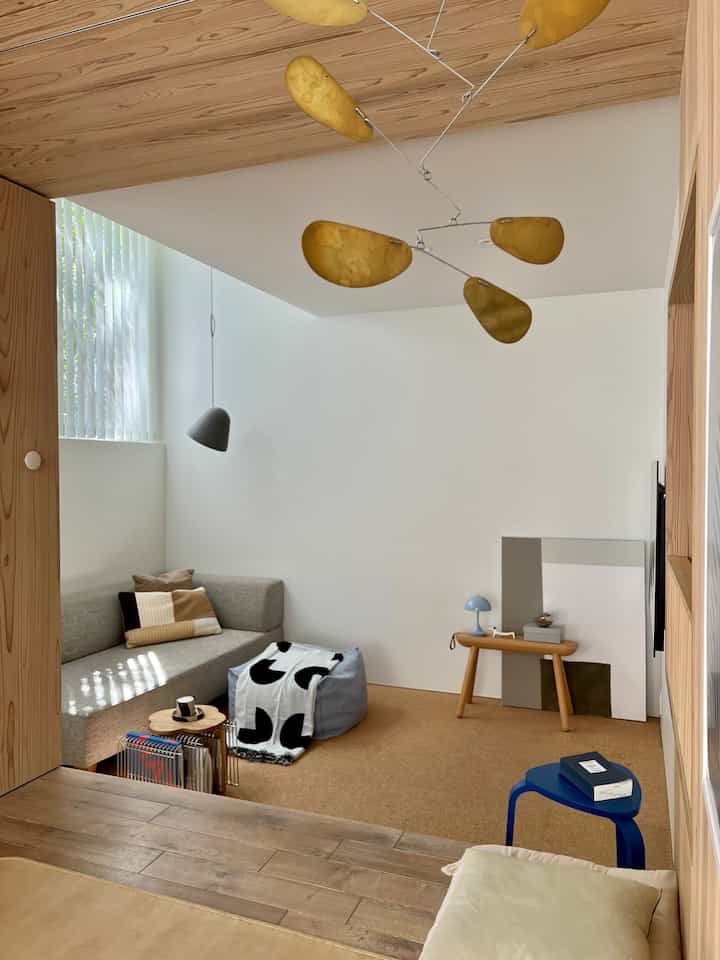 ナチュラルな色調のコンパクトなリビング、コルクマットと快適なソファ、木製スツールが配置された落ち着いた空間