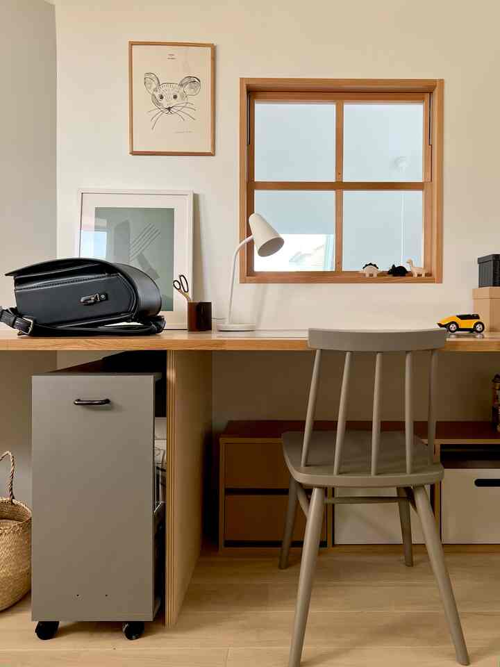 ナチュラルトーンの子供部屋、木製のデスクと椅子、テーブルランプが配置された落ち着いた印象的な空間