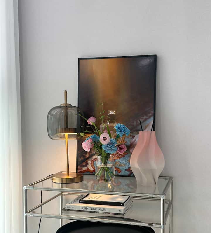 白い壁を背景にしたミッドセンチュリーモダンスタイルのインテリア、金属製棚の上にテーブルランプや花瓶、ピンクのワイングラスが調和よく配置されている雰囲気のある空間