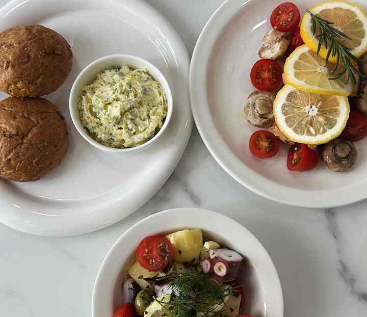 白いテーブルトップに白いトレイと皿が配され、中央に多彩な地中海風料理とバターのラムキンボウルが置かれたインテリア