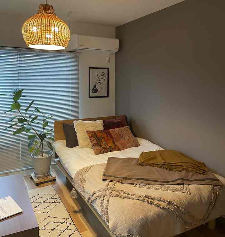 ナチュラルな木目調とブラウンのクッションが配された寝室、セミダブルベッドと観葉植物が置かれた雰囲気のあるインテリア