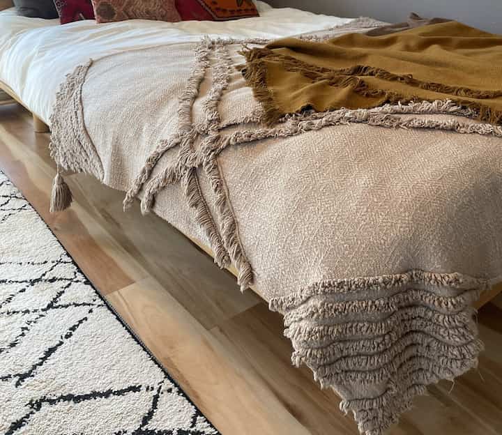 ベージュとブラウンの色調の寝室、ベッドに重ねられたブランケットとクッションがある雰囲気のあるボヘミアン風インテリア