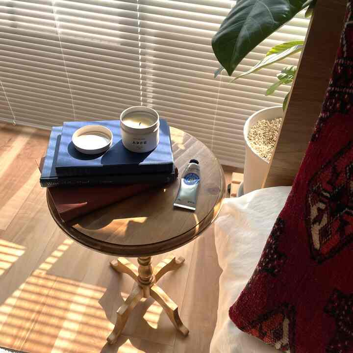 ウッドトーンとネイビーが調和した寝室に、木製の丸いサイドテーブルがあり、キャンドルとハンドクリーム、ヴィンテージの洋書が置かれた雰囲気のあるインテリア