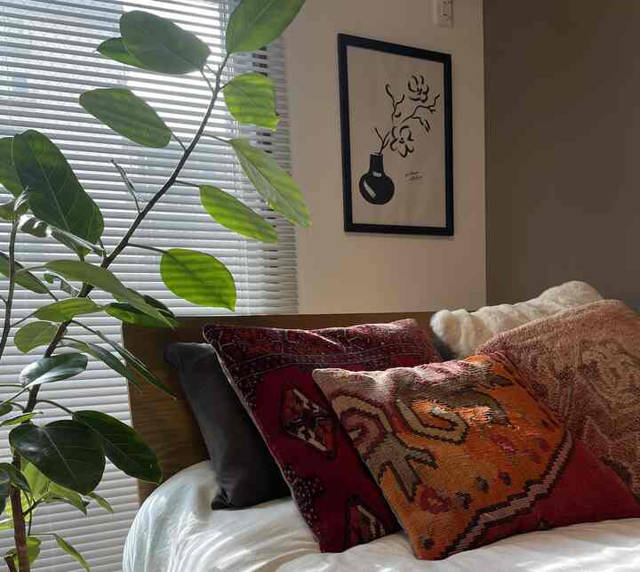 ナチュラルな色調の寝室、木製フレームのベッドとボヘミアンスタイルのクッションが配置された落ち着いた雰囲気のインテリア