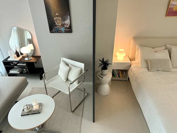 ホワイトとベージュのトーンで分かれたリビングと寝室、居心地の良い家具と温かみのある照明があるシンプルモダンなインテリア