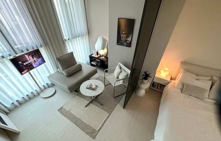 ホワイトとベージュのトーンが特徴のワンルーム、リビングと寝室が配置されたミニマルでコンパクトな印象的な空間